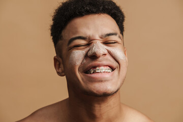 Obraz premium Young shirtless man with cosmetic clay mask smiling at camera