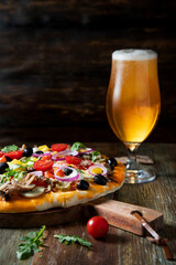 Homemade pizza with vegetables and a glass of beer on a rustic table
