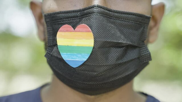 close up shot of man with pride or rainbow heart symbol on medical face mask during coronavirus covid-19 pandemic pride march - concept of solidarity, pride celebrations