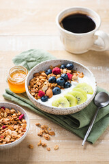 Healthy breakfast with cup of coffee and granola bowl with greek yogurt, blueberries and kiwi on a wooden table