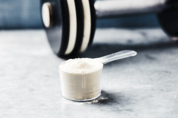 Scoop of Whey Protein and a dumbbell. Bodybuilding food supplements on stone background. Soft focus. Close up. Copy space.