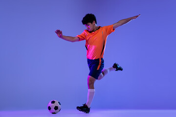 Studio shot of male professional football, soccer player practicing with ball isolated on purple background. Concept of sport, match, active lifestyle, goal and hobby