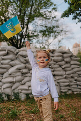 Ukrainian girl wave Ukrainian flag in her hand and ukrainian flag painting on her face in front of military barrier