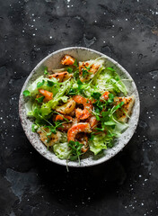 Caesar salad with grilled shrimp on a dark  background, top view