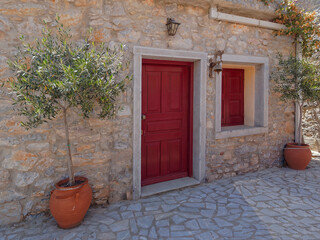 An old stone house front with a red painted wooden door, window and potted plant. Pyrgi, Chios island, Greece.