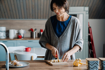 Fototapeta na wymiar White mature woman smiling while making breakfast in kitchen