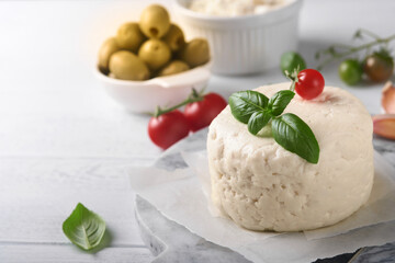 Ricotta cheese. Homemade Ricotta cheese with basil, garlic, tomatoes and green olives on parchment paperback and stand. Italian food.  Selective focus.