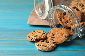 Overturned glass jar with delicious chocolate chip cookies on turquoise wooden table, closeup. Space for text