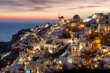 Santorini famous view with white houses and windmill during sunset. Vacation in Greece on the Aegean sea.