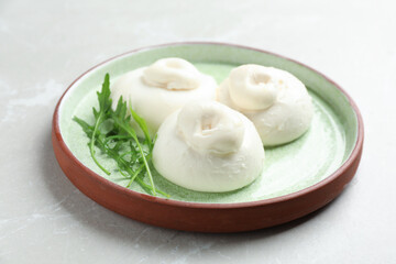 Delicious burrata cheese with arugula on light table, closeup