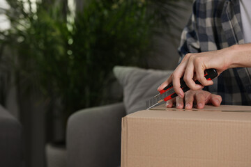 Man using utility knife to open parcel at home, closeup. Space for text