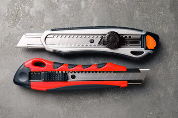 Different utility knives on grey table, flat lay. Construction tool