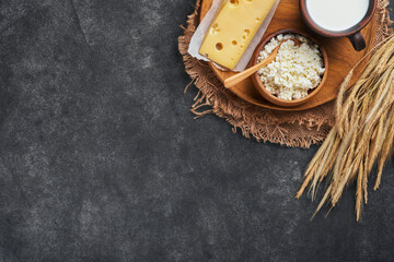 Happy Shavuot. Background for Shavuot traditional religious Jewish celebration. Milk and cheese, ripe wheat and fruits. Dairy products over old dark grey background. Shavuot concept. Top view. Mock up