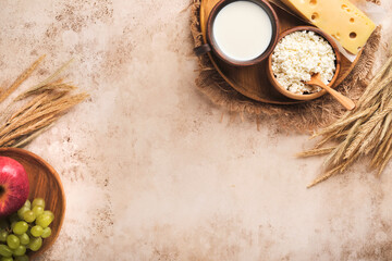 Happy Shavuot. Background for Shavuot traditional religious Jewish celebration. Milk and cheese, ripe wheat and fruits. Dairy products over old light brown wall background. Shavuot concept. Top view.
