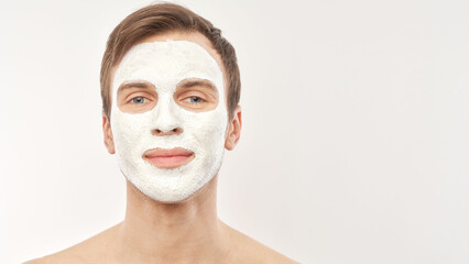 Portrait of young handsome man with cosmetic mask on his face isolated on white background