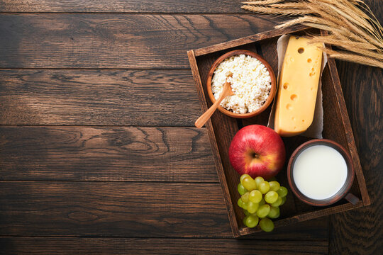 Happy Shavuot. Background for Shavuot traditional religious Jewish celebration. Milk and cheese, ripe wheat and fruits. Dairy products over old brown wooden background. Shavuot concept. Top view.