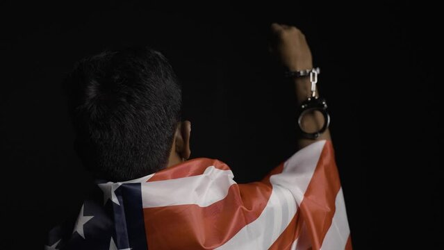 back view shot of man with us or american flag on shoulder showing hands with released cuffs on black background