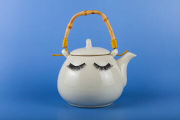 White teapot with eyes on a blue background.