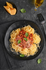 Classic spaghetti pasta Bolognese. Tasty appetizing italian spaghetti with bolognese sauce, tomato sauce, cheese parmesan and basil on black plate on dark stone or concrete table background. Top view.