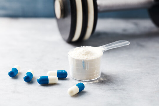 Scoop of Whey Protein and creatine capsules  on stone background. Close up.