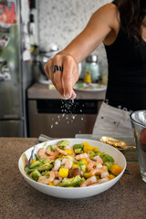 Female hand adding salt to avocado and shrimp salad in a bowl. Seasoning ready meal by sprinkling...
