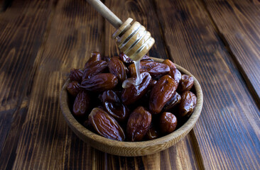 Dates in the bowl and honey on the wooden background. Close-up.