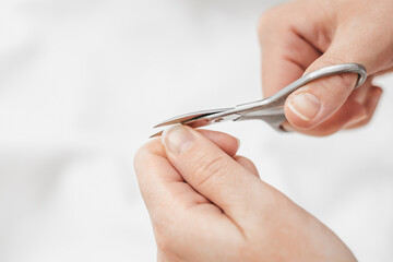 Nail care at home. A woman's hand cuts nails with manicure scissors on a white background. Nail hygiene. Hand care. copy space
