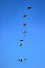 Military parachutist paratroopers parachute jumping out of a air force planes on a clear blue sky day.