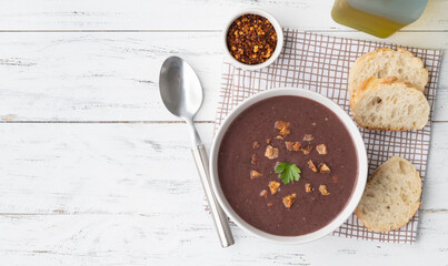 Black bean soup in a bowl with bread slices and seasoning over wooden table with copy space