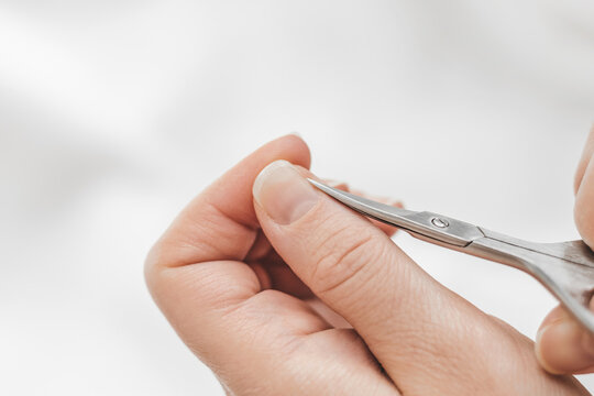 Trims cuticles on fingers. Home manicure. A woman's hand cuts nails with manicure scissors on a white background. Nail hygiene. Hand care