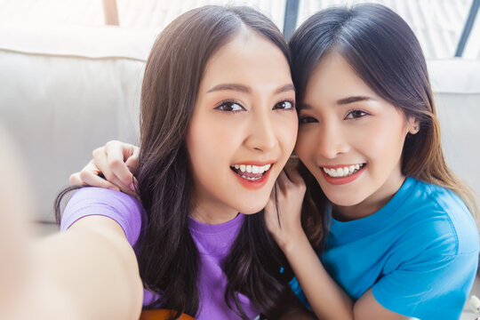 Two happy young women friends  looking at camera of smart phone making selfies on mobile phone with happiness and smile face Portrait of happy girl friend Older sister and younger sister stay at home