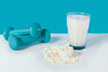 Glass of protein shake, protein powder in the spoon and blue dumbbells on a blue background.
