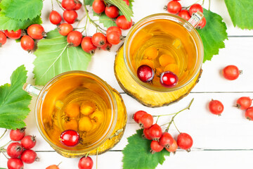 Two cups of hawthorn tea on wooden stands and clusters of hawthorn berries on a light pink wooden background. Traditional medicine.