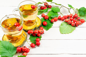 Two mugs of delicious hot tea (infusion) of red ripe hawthorn, twigs and berries with green leaves on a pink wooden background. Space for text.