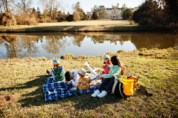 Mother with four kids having picnic near pound at Lednice park against castle, Czech Republic.