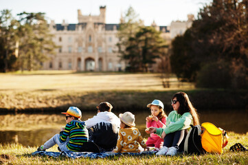 Mother with four kids having picnic near pound at Lednice park against castle, Czech Republic.