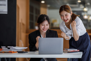 Fototapeta premium Euphoric winner watching a laptop on a desk winning at working in an office, Asian Teamwork, coworker cooperation, financial marketing team, or corporate business employee concept.