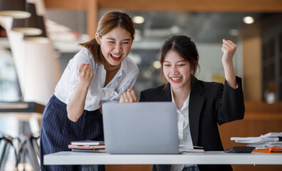 Euphoric winner watching a laptop on a desk winning at working in an office, Asian Teamwork, coworker cooperation, financial marketing team, or corporate business employee concept.