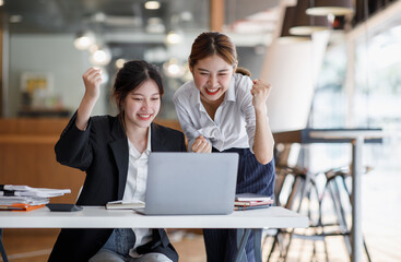 Euphoric winner watching a laptop on a desk winning at working in an office, Asian Teamwork, coworker cooperation, financial marketing team, or corporate business employee concept.
