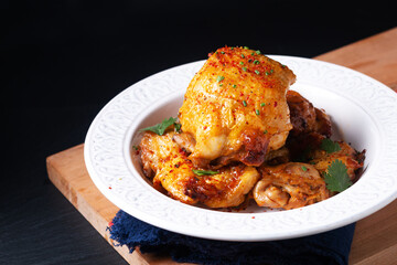 Food concept Roasted spicy chicken thighs on ceramic plate on wooden board with black background with copy space