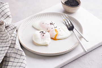 Three poached eggs with egg yolk dripping and black sesame seeds on a white plate on a marble board and silver forks