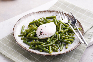 Soft-boiled poached eggs with black sesame seeds on a cooked green beans on a plate with brown rim on a green checkered kitchen towel