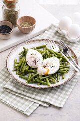 Soft-boiled poached eggs with black sesame seeds on a cooked green beans on a plate with brown rim on a green checkered kitchen towel