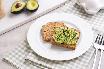 Slices of gluten-free sunflower seeds bread with avocado and sesame seeds on white plate on green checkered napkin