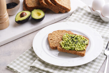 Slices of gluten-free sunflower seeds bread with avocado and sesame seeds on white plate on green checkered napkin