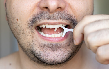 Obraz premium young man is cleaning his teeth with a toothpick. plastic dental floss. close up photo of mouth. stomatological concept. dental care, family education. Beard man