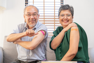 Coronavirus Vaccination, happy asian elderly, aged family smile strong together, showing bandage on arm with protect of covid-19 after injection of vaccine, sitting on couch in living room at home.