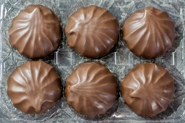 An airy marshmallow in chocolate glaze in a box close-up on a black background.