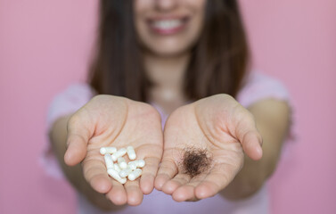 hair loss problem and treatment concept. young woman with a white pill, capsules, in one hand and a ball of fallen hair in another. smiling girl on pink background. lack of vitamins, minerals - obrazy, fototapety, plakaty