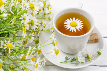Tea (decoction, infusion) from chamomile medicinal (pharmacy) field in a cup on a saucer on a white wooden background. Medicinal herb Matricaria, herbal medicine.